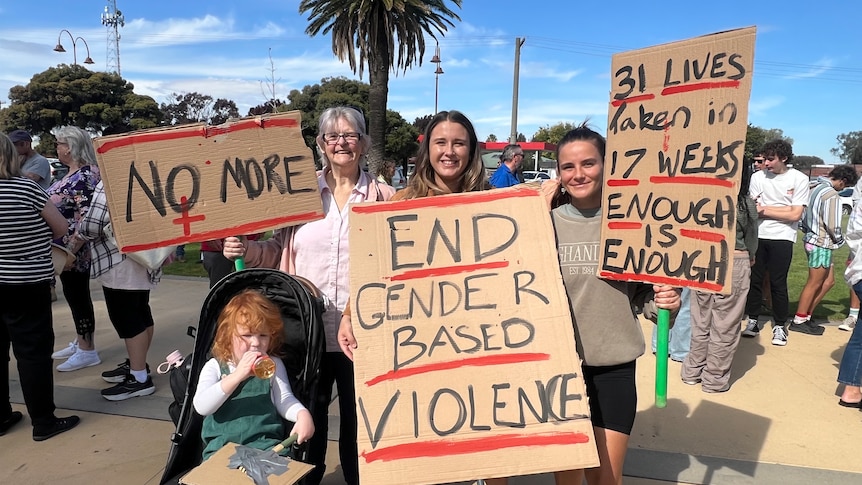 Three women holding up signs protesting violence against women