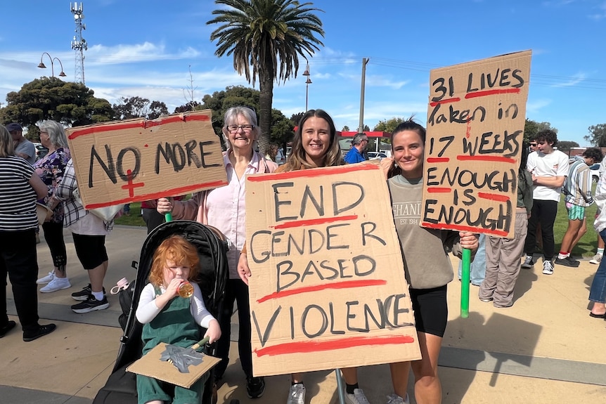 Three women holding up signs protesting violence against women