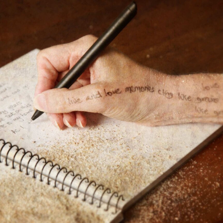 A hand holding a pen and writing in a notebook covered in sawdust