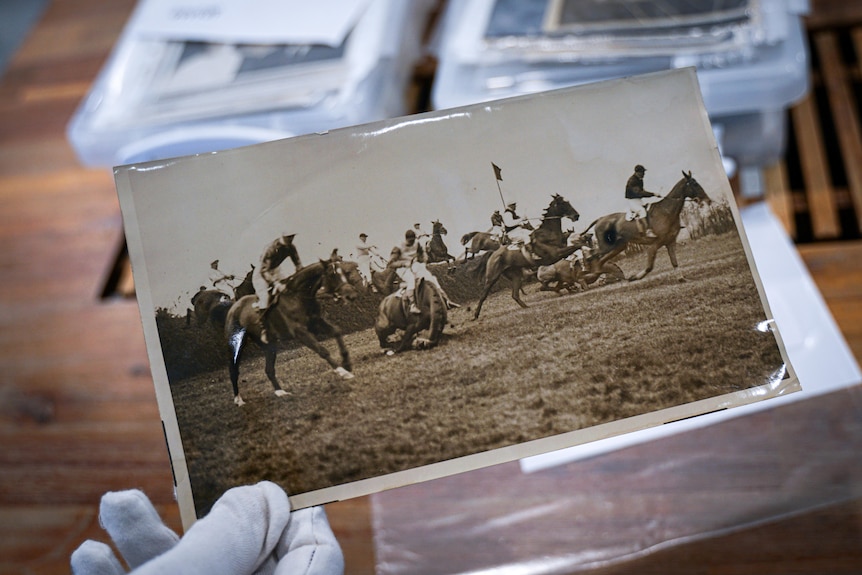 A hand holding a photograph of an old horse race.