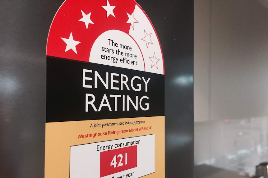Close up of energy star rating sticker on chrome refrigerator, microwave and kettle in background.