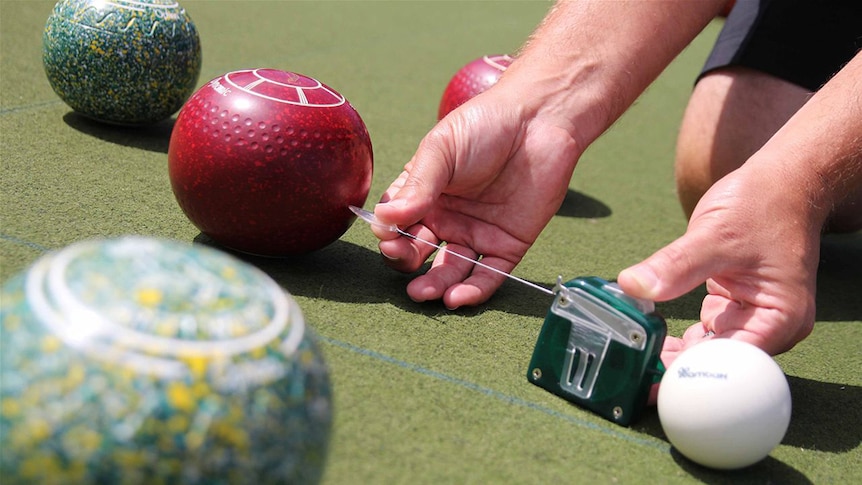 A pair of hands measures the distance between a lawn bowl and the jack