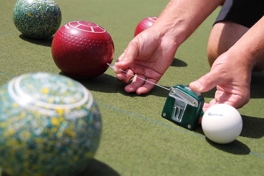 A pair of hands measures the distance between a lawn bowl and the jack
