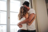 Man and woman embrace standing up in a story about how to support your partner if they experience pain during sex.