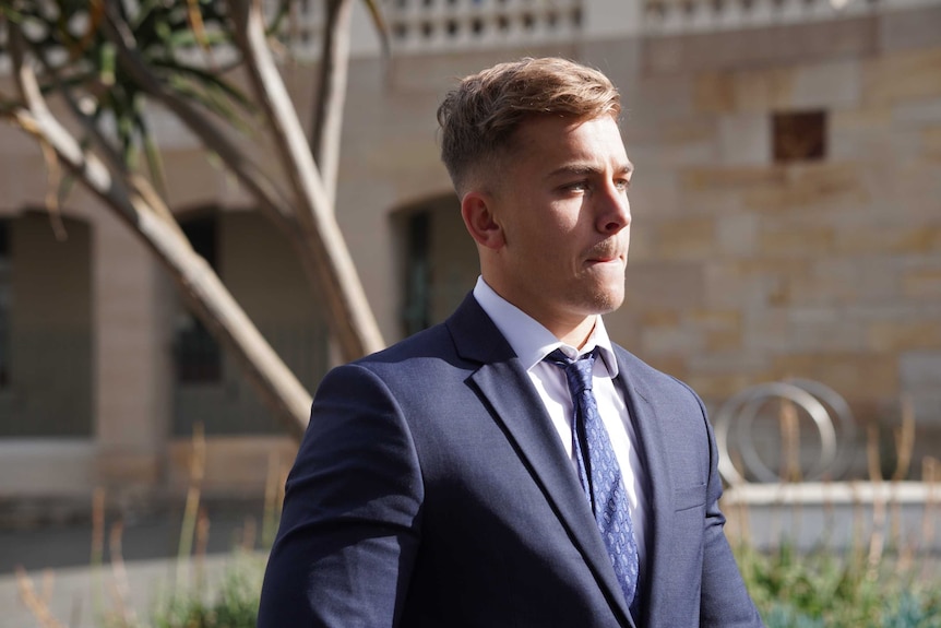 A young man in a dark suit walking near a court building.