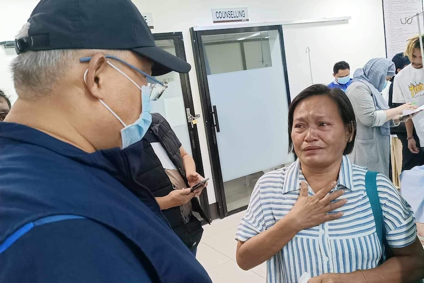 A woman holds her hand on her chest crying, speaking to a man at a medical facility. 