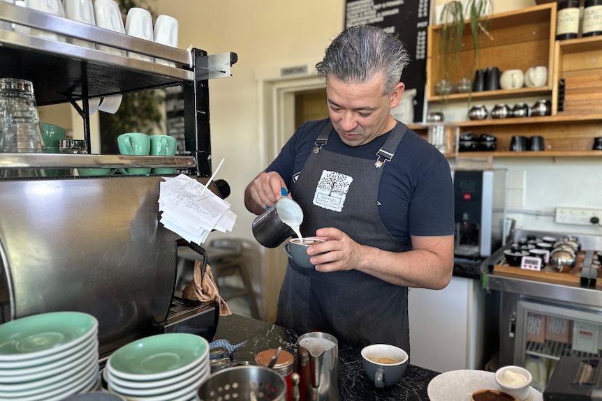 A man in an apron makes a coffee in a cafe.