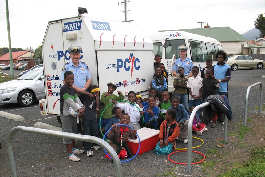Police officers and children around a PCYC trailer.