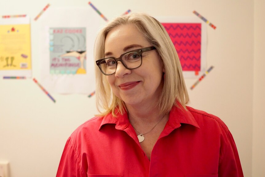 Writer Kaz Cooke smiles while looking at the camera. She's wearing a red blouse and eye glasses.