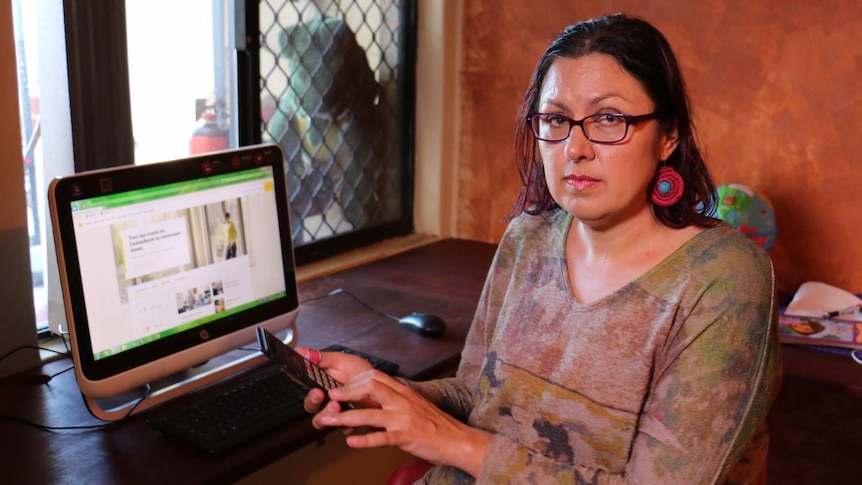 Woman sitting in front of computer and holding phone, looking worried