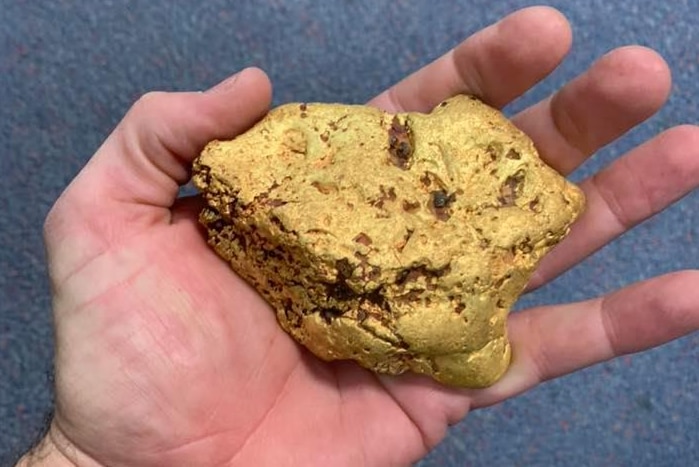 A large gold nugget held in the palm of a man's hand.