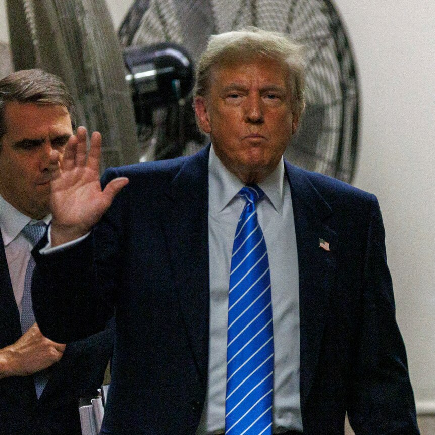 Donald Trump waves while walking toward the camera as he is followed by two men in suits