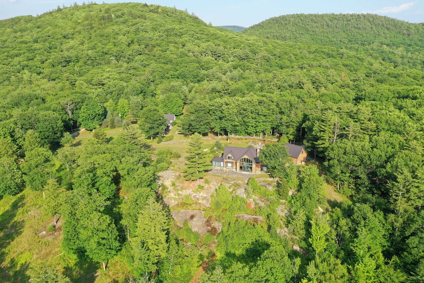 An aerial image of a house hidden away in amid forested hills.