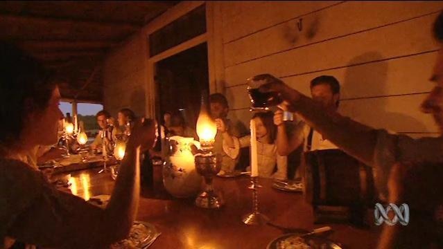 People sit around table by candlelight, raise glasses to toast