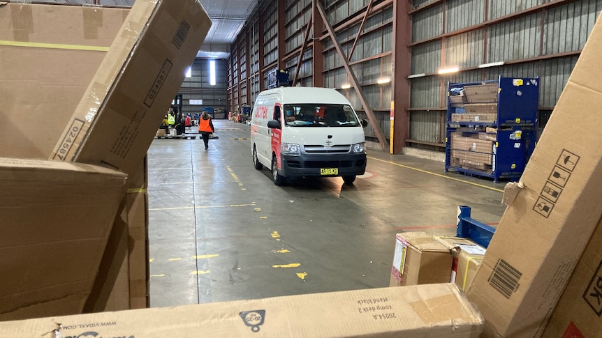 A delivery van in a warehouse, with boxes stacked in front.