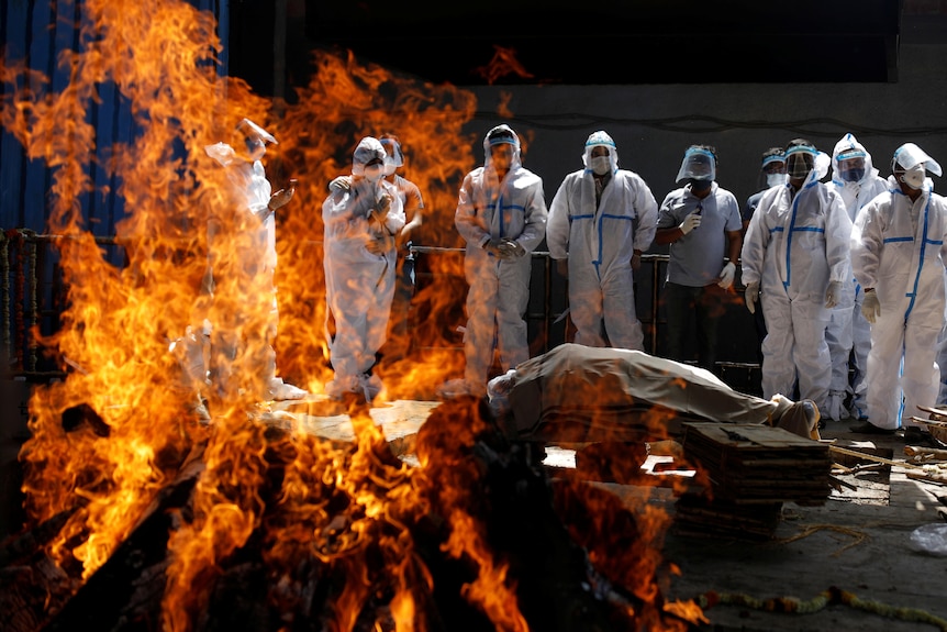 Relatives wearing personal protective equipment attend the funeral of a man seen burning before them.