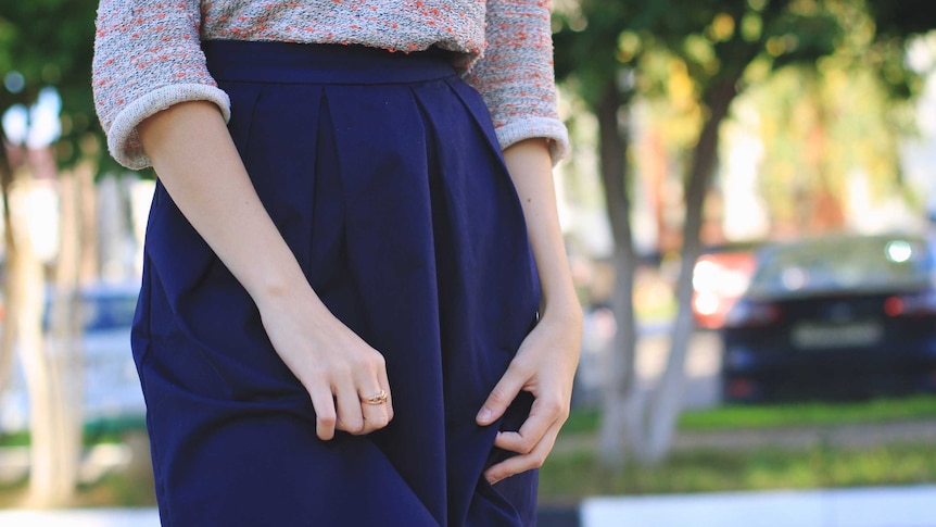 A woman's hands pluck at her long dark skirt.