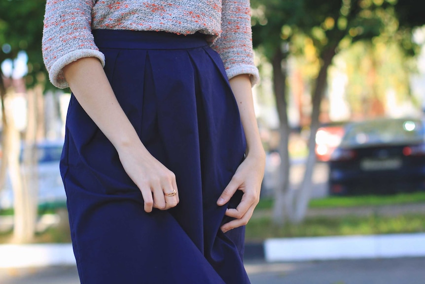 A woman's hands pluck at her long dark skirt.