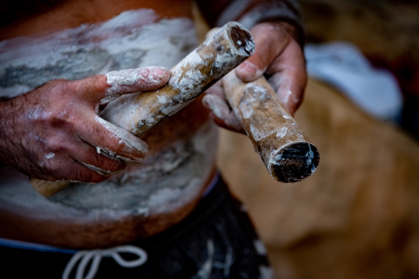 A man's hands, painted with white paint, play the rhythm sticks.