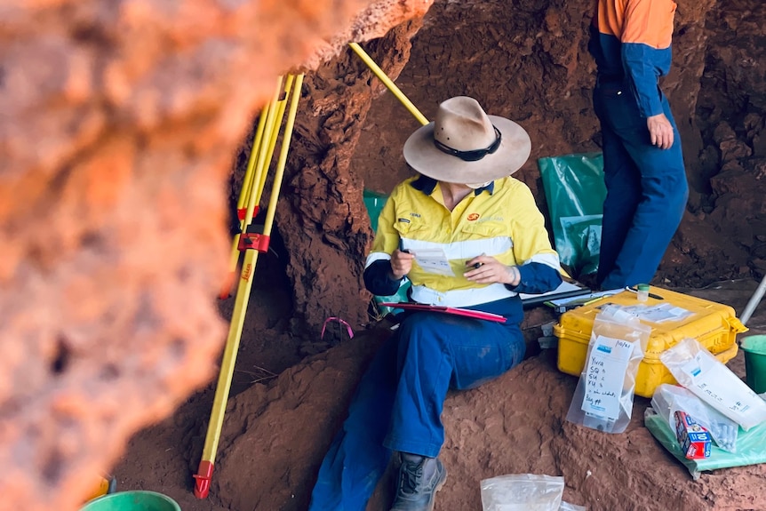 A female archaeologist in high viz sits inside a rock shelter