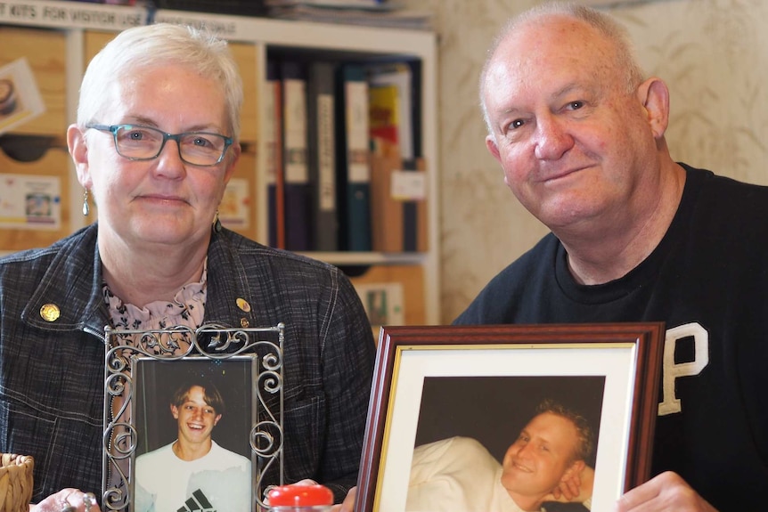 A man and a woman holding framed photos of two men