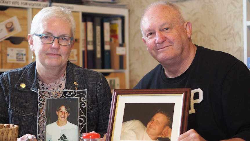 A man and a woman holding framed photos of two men