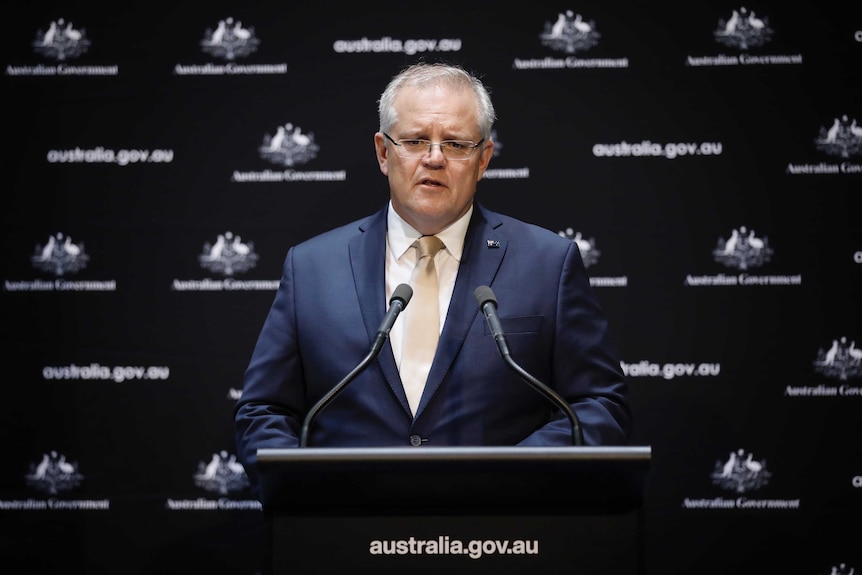 Prime Minister Scott Morrison stands at a podium with microphones in front of him, he is wearing a suit.