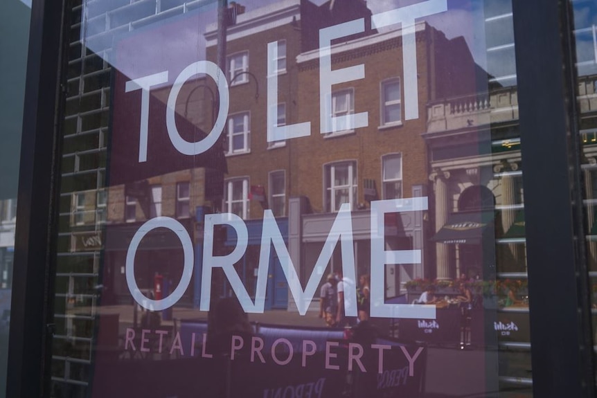 A sign in a UK shopfront indicates it is up for rent, buildings are reflected in the window.