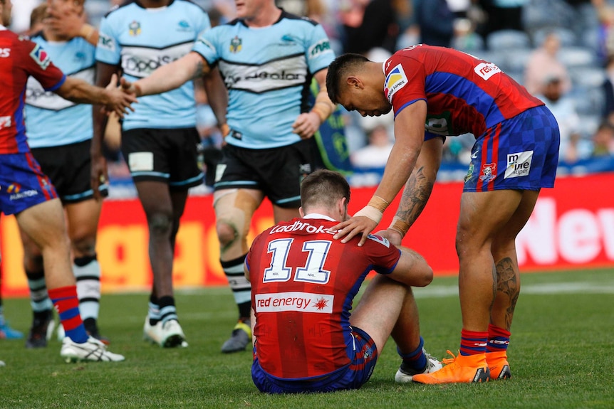 Lachlan Fitzgibbon sits on the ground and is consoled by Ken Sio after the Knights lost to the Sharks.