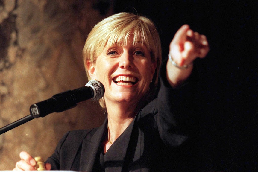 A woman smiles and points while speaking into a microphone