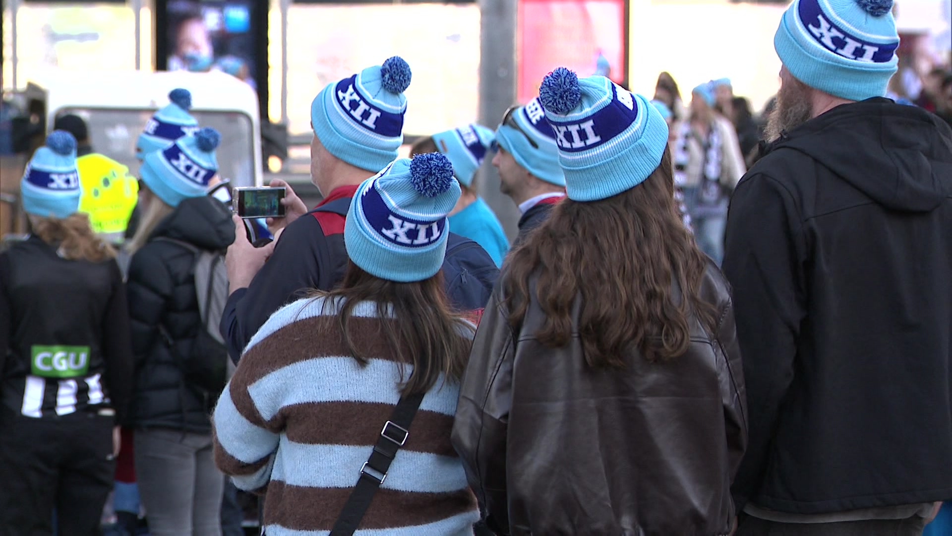 A photo taken from people wearing the same blue two-toned beanie with the roman numeral for 12.