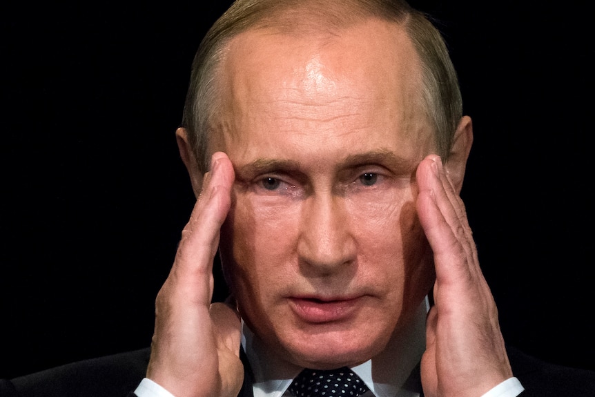 Vladimir Putin holds his fingers to his temples 