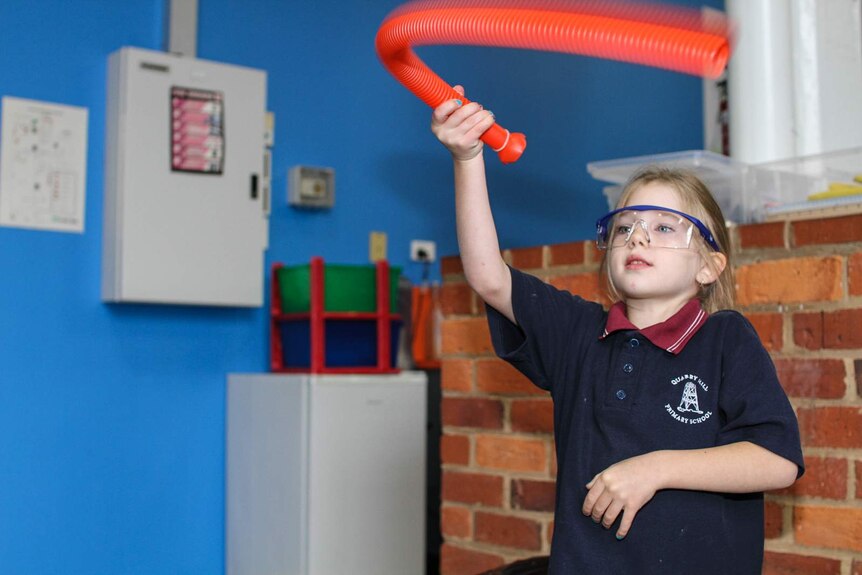 A young primary school student twirls a plastic tube to understand different sources of sounds.