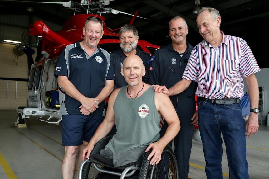 Former pilot and rescue crewmen pictured beside Warren in front of a helicopter in Cairns