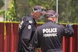 A photo of two forensics officers inspecting a red corrugated fence.