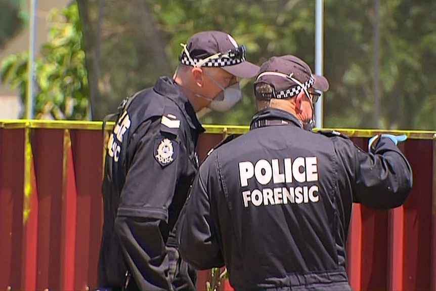 A photo of two forensics officers inspecting a red corrugated fence.