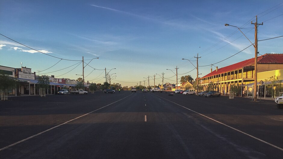 A wide shot of a very wide street of a country town with a very large old hotel on one side with a big verandah