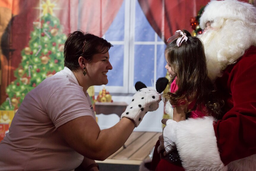A hand puppet is used to get a smile from a little girl on Santa's knee.