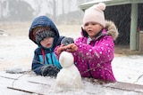 two children in colorful jackets building a snowman on a picnic table