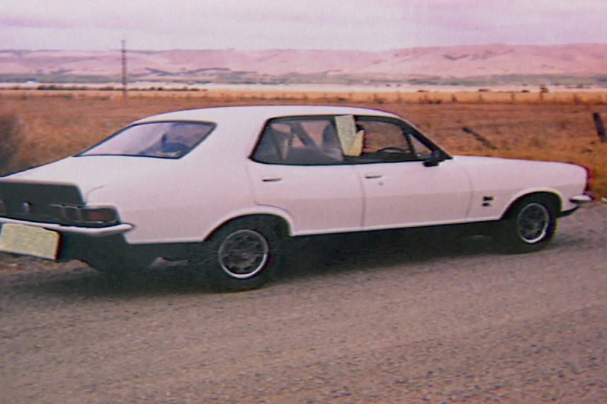 A white Torana sedan parked on a dirt road