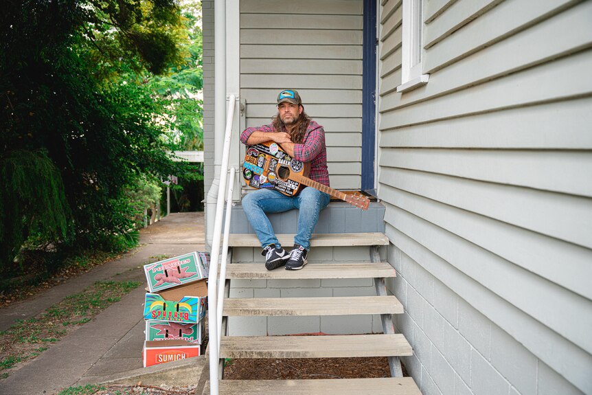 James poses at top of the back steps of his house, with a guitar on his lap