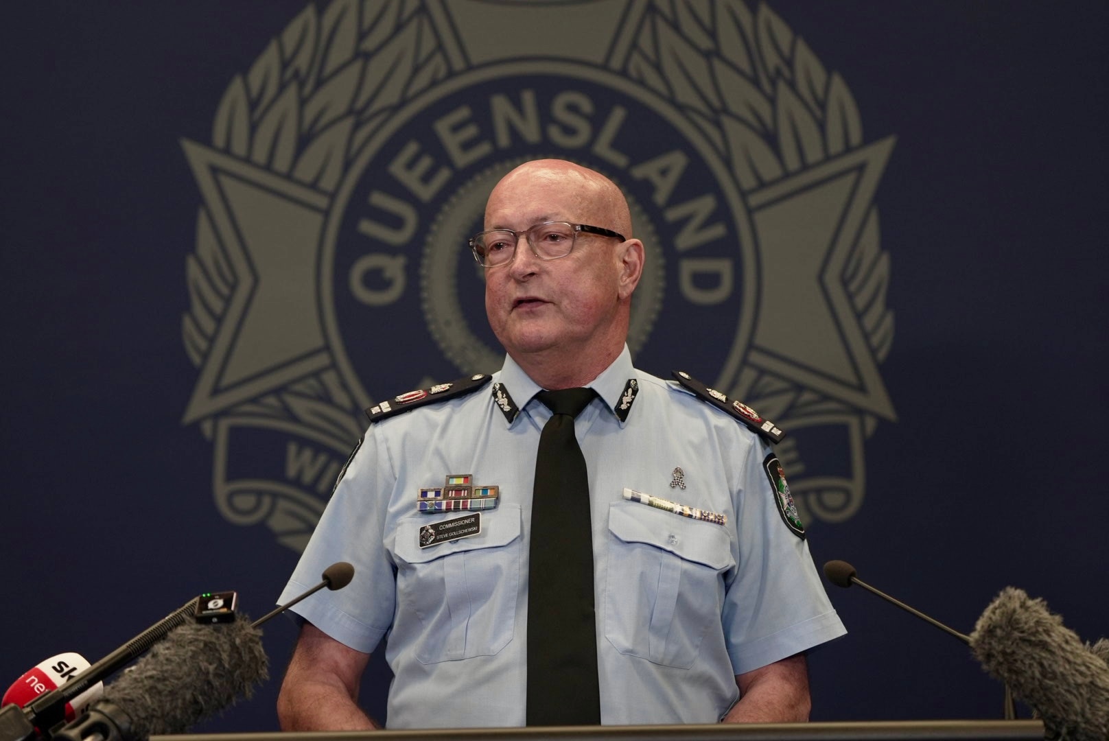 Steve Gollschewski está atrás de um microfone com o logotipo da Polícia de Queensland atrás dele.