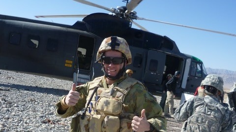 Man in Australian combat protection giving thumbs up in front of black helicopter.