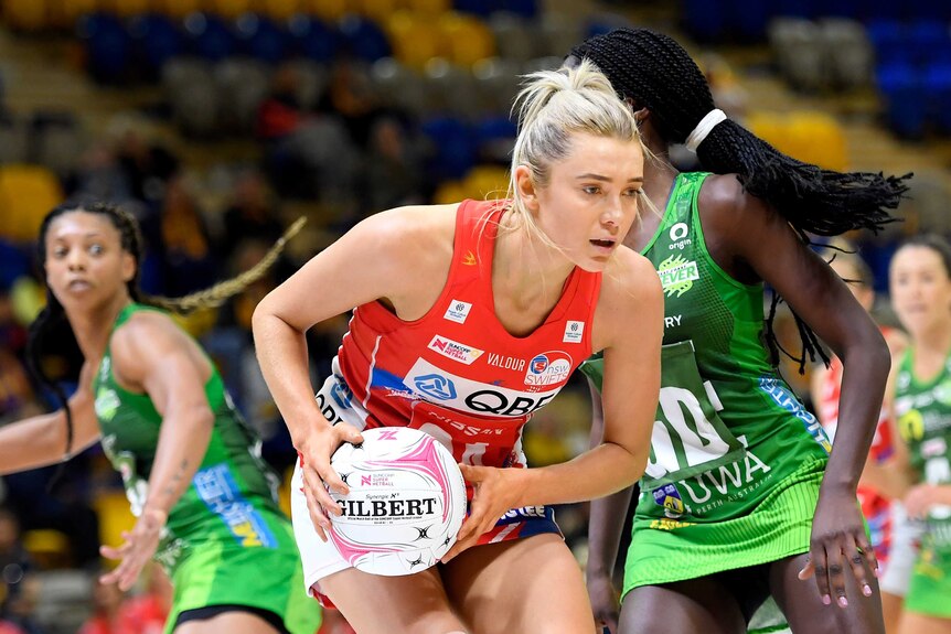 A NSW Swifts Super Netball player holds the ball in two hands against the West Coast Fever.