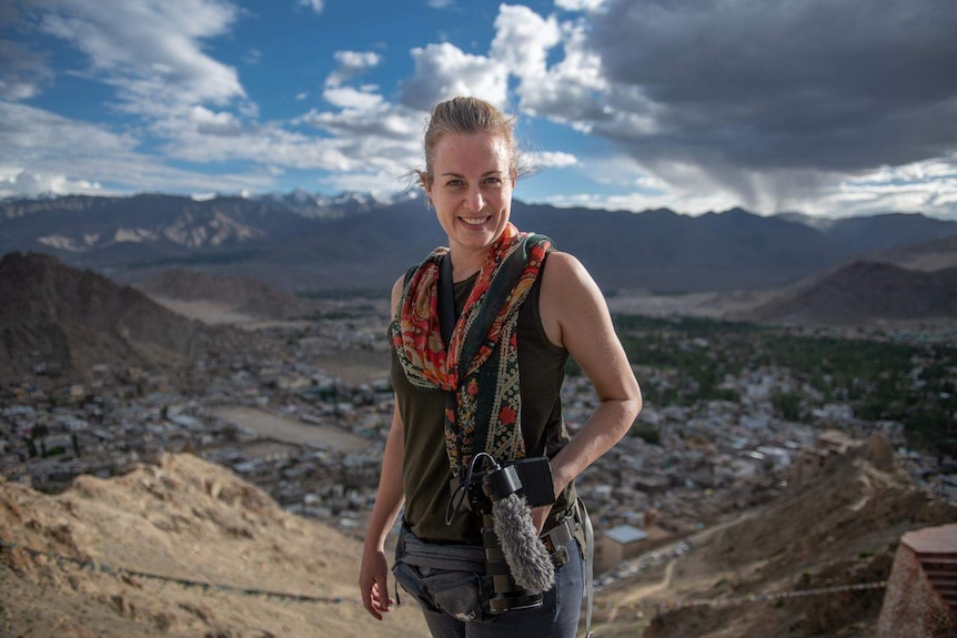 Heanue standing at top of mountain with ranges in background and dark stormy sky.