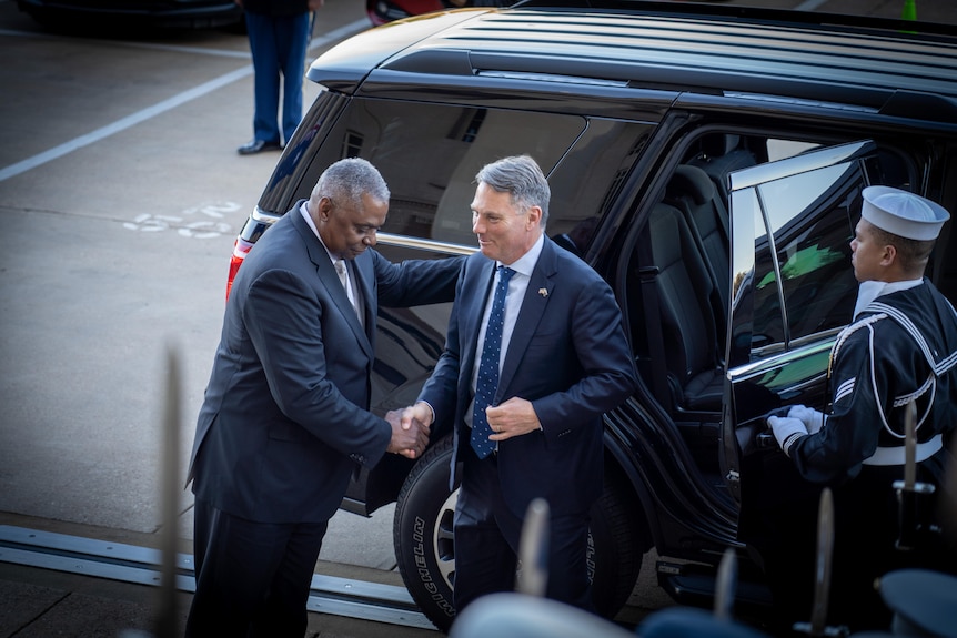 Lloyd Austin and Richard Marles shake hands in front of a car