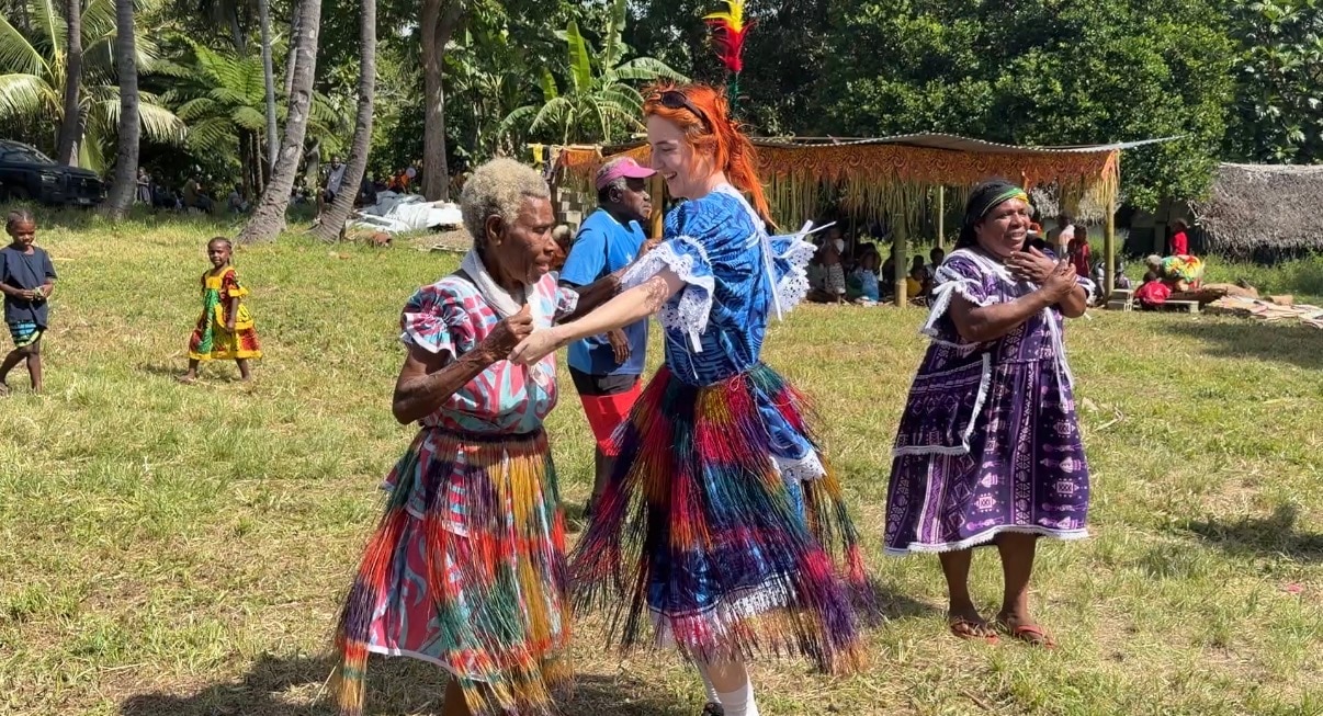 Kate dances with a woman in a field in Vanuatu.