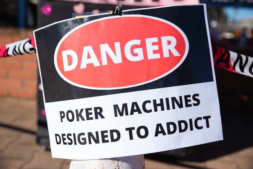 A red, black and white sign that says Danger, Poker machines designed to addict.