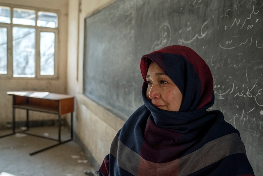 An Afghan teacher cries as she stands in an old classroom.