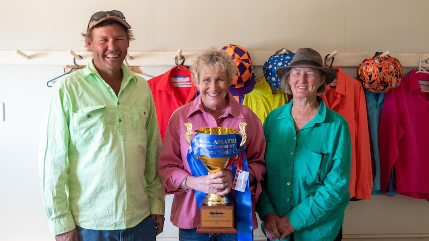 Two women and one man smiling and holding a large gold cup with ribbon on it that reads Brunette Downs